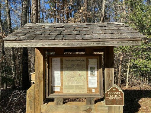 A wooden information kiosk in a forest, featuring a map and details about Oconee Station.