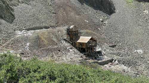 Abandoned wooden structure on a rocky hillside, surrounded by debris and vegetation.