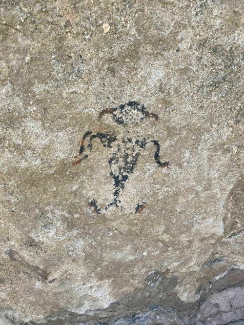 Ancient rock painting depicting a humanoid figure with outstretched arms on a textured stone surface.