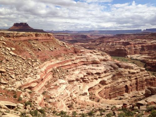 A vast canyon landscape with layered red rock formations and a cloudy sky in the background.