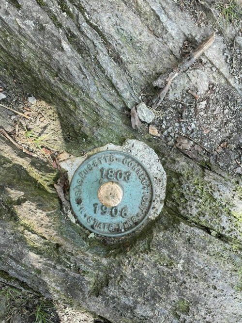 A metal survey marker embedded in a rock, inscribed with "Massachusetts 1803 1906."