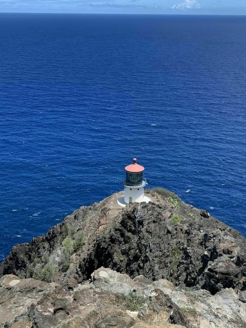 A lighthouse perched on a rocky cliff overlooking a vast blue ocean under a clear sky.