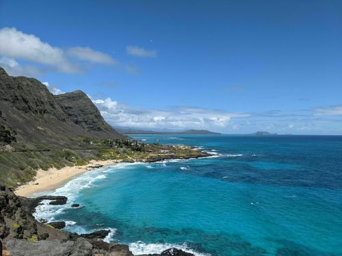 A scenic view of a coastline with turquoise waters, sandy beach, and mountains under a clear blue sky.