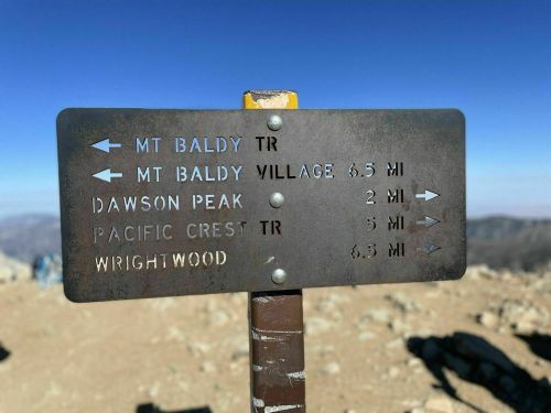 Trail sign at a mountain summit indicating distances to Mt. Baldy, Dawson Peak, Pacific Crest Trail, and Wrightwood.