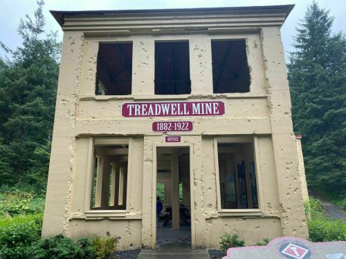 Historic Treadwell Mine building, with peeling paint and large windows, surrounded by trees. Dates: 1882-1922.
