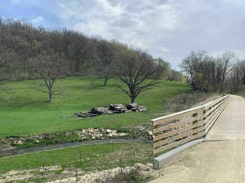 A wooden bridge crosses a small stream, with a grassy hill and bare trees in the background.