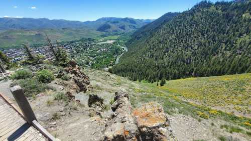 A scenic view of a valley surrounded by mountains, with a small town and a river visible below. Bright blue sky above.