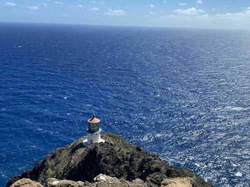 A lighthouse perched on a rocky cliff overlooking a vast blue ocean under a clear sky.