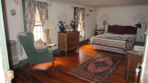 Cozy bedroom with a bed, wooden furniture, floral curtains, and a patterned rug on polished wooden floors.