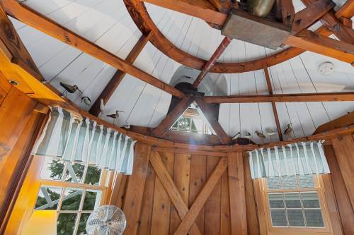 Interior view of a wooden room with a circular ceiling, beams, and light streaming through a triangular window.