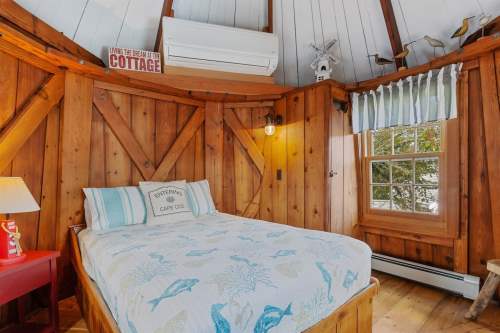 Cozy wooden bedroom with a double bed, lamp, and window, featuring rustic decor and a warm atmosphere.