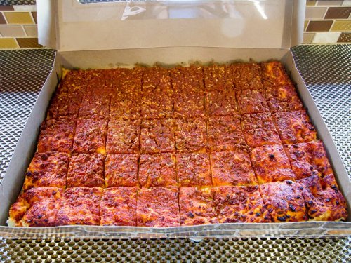 A large pizza in a box, cut into square slices with a crispy, golden-brown topping.
