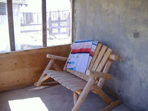A rustic wooden bench with a colorful blanket draped over it, set against a simple, unfinished wall.