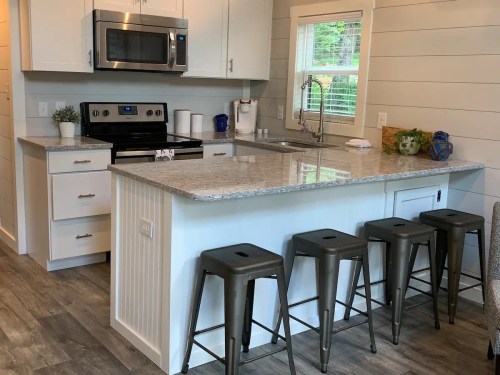 Modern kitchen with white cabinets, stainless steel appliances, and a granite island with metal stools. Bright and inviting space.