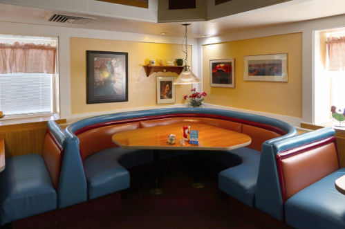 Cozy diner interior featuring a curved booth, wooden table, and warm lighting with decorative wall art.