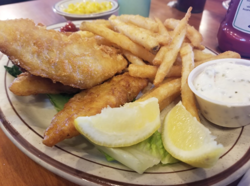 A plate of crispy fried fish fillets, golden fries, lemon wedges, and a side of dipping sauce.