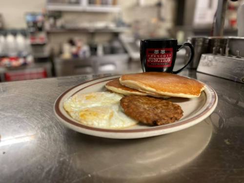 A plate with pancakes, eggs, and sausage, alongside a coffee mug on a diner counter.