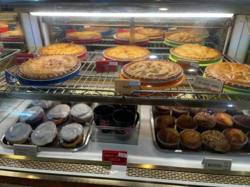 A display case filled with various pies and muffins, showcasing colorful plates and labels for each item.