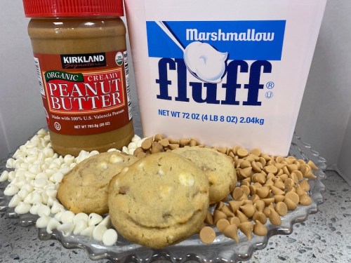 A plate with cookies, white chocolate chips, peanut butter, and a container of marshmallow fluff.