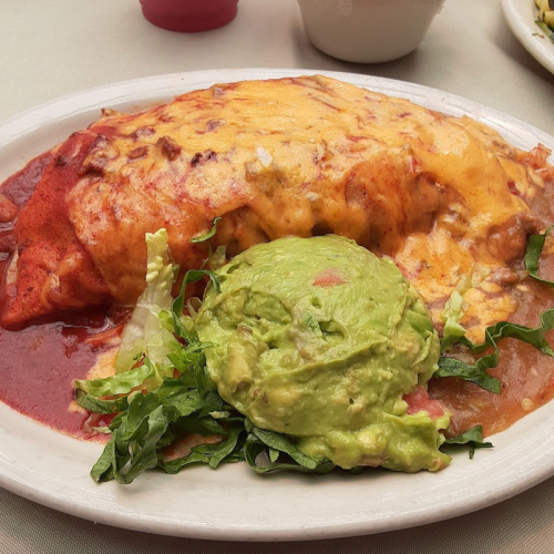 A plate of enchiladas topped with melted cheese, served with guacamole and fresh lettuce on the side.