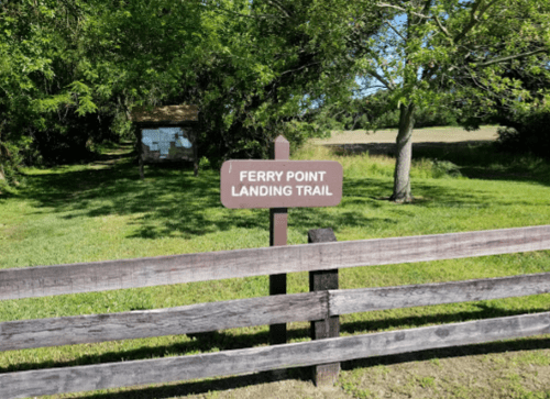 Sign for Ferry Point Landing Trail in a green, grassy area with trees in the background.