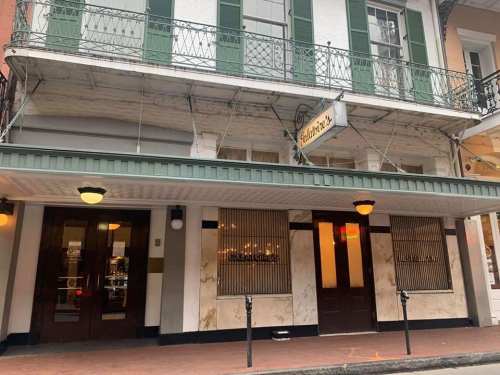 Exterior of a restaurant with green shutters, a sign, and decorative ironwork, located on a city street.