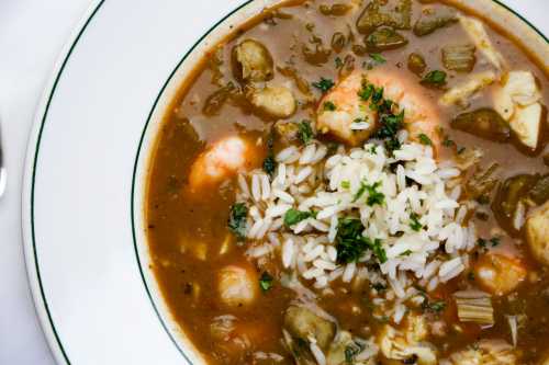 A bowl of gumbo with shrimp, vegetables, and rice, garnished with fresh herbs.