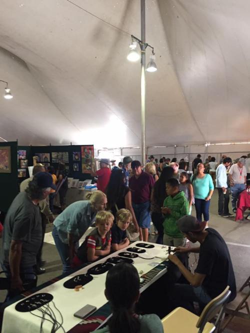 A busy indoor market scene with people browsing art and crafts under a large tent.