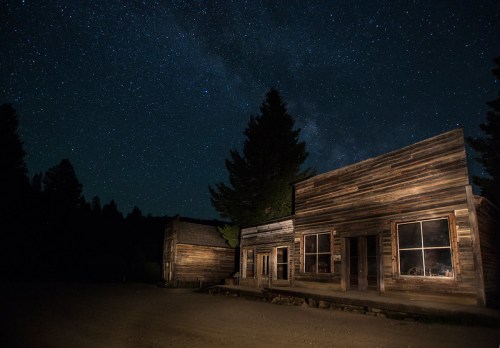 A rustic wooden building under a starry night sky, with trees silhouetted in the background.