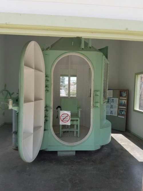 A large, green chamber with a round door, inside a museum setting, featuring a sign that says "No Smoking."