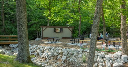 A picnic area with tables near a small building, surrounded by trees and rocky landscaping.