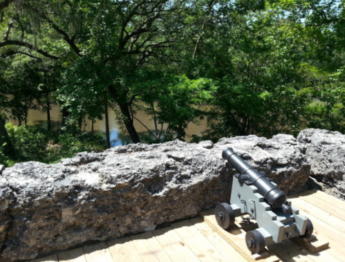 A historic cannon on a stone wall overlooking a lush green landscape and a river.