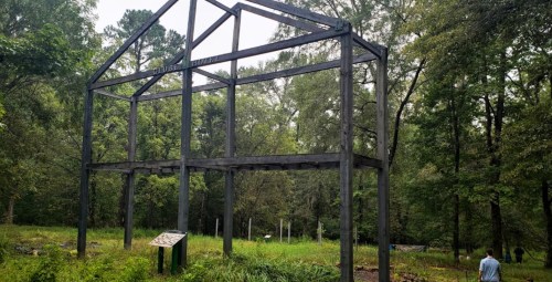 A partially constructed wooden frame of a building in a lush green forested area.