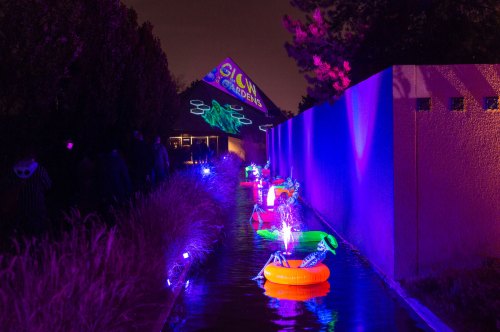 A brightly lit pathway with colorful inflatable rings and glowing decorations, set in a garden at night.