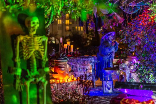 A colorful Halloween scene with a skeleton, candles, and a figure in a witch's hat surrounded by vibrant decorations.