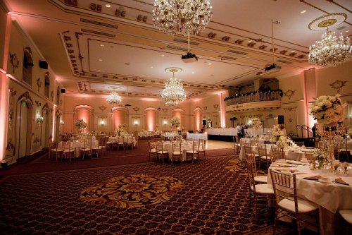 Elegant banquet hall with chandeliers, round tables set for dining, and soft lighting creating a warm atmosphere.