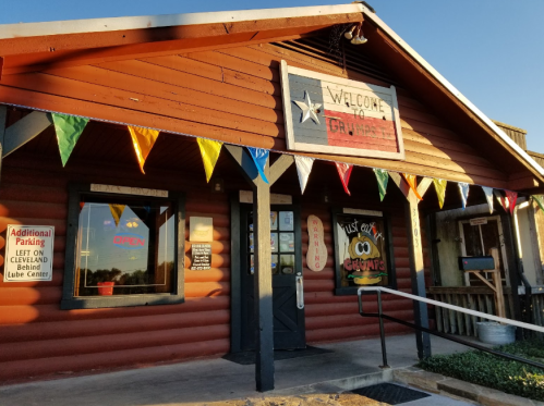 A rustic building with a sign reading "Welcome to [Name]" and colorful flags, indicating it's open for business.