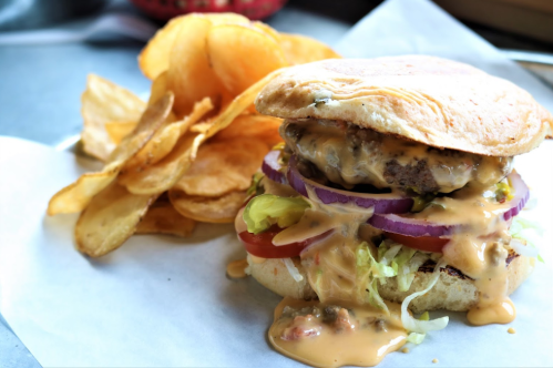 A juicy burger with melted cheese, lettuce, tomato, and onion, served with a side of crispy potato chips.