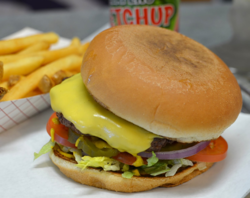 A cheeseburger with lettuce, tomato, onion, and a side of fries, served on a white paper tray.