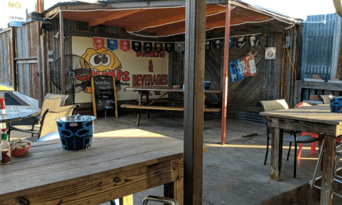 Outdoor seating area of a casual eatery with wooden tables, colorful decor, and a sign for burgers and beverages.