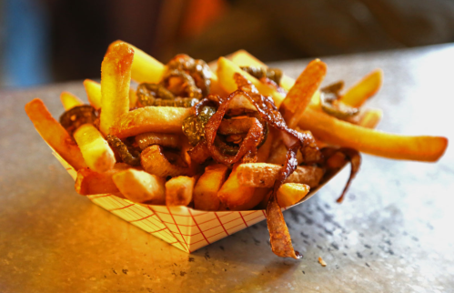 A serving of golden French fries topped with crispy onions in a paper tray.
