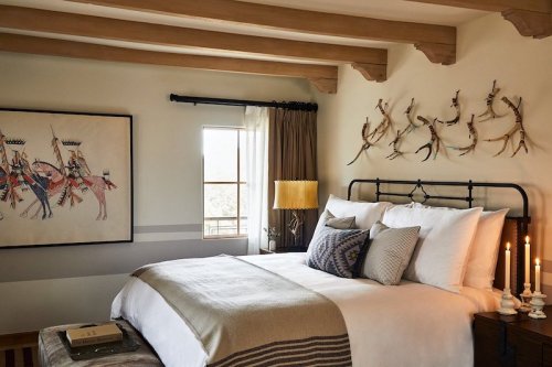 Cozy bedroom with a bed, decorative wall art, and soft lighting from a lamp and candles. Warm, inviting atmosphere.