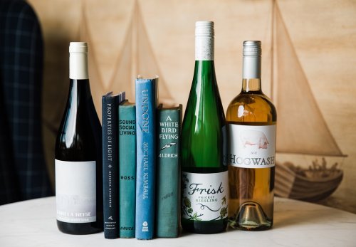 A selection of wine bottles next to a stack of books on a table, with a nautical-themed background.