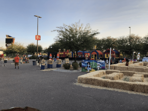 A festive outdoor scene with hay bales, a bounce house, and decorations, set in a parking lot under a clear sky.