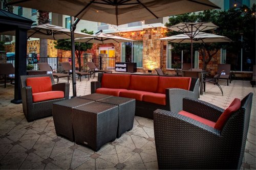 Outdoor seating area with a red and black wicker sofa set, surrounded by umbrellas and greenery.