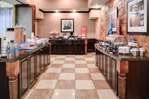 A hotel breakfast area featuring a buffet with various food items, coffee machines, and a checkered floor.