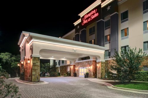 Exterior view of a Hampton Inn & Suites at night, featuring a well-lit entrance and landscaped surroundings.