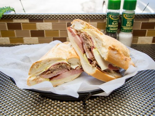 A close-up of a sandwich with layers of meat and cheese, served on a plate with salt and pepper shakers in the background.