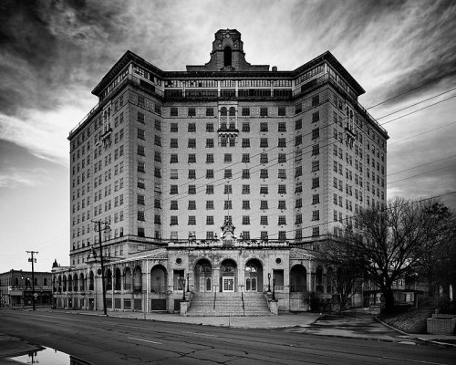 A large, historic hotel building in black and white, featuring ornate architecture and a cloudy sky.