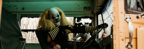 A creepy clown with wild hair drives a dilapidated bus, surrounded by unsettling dolls and a dark atmosphere.